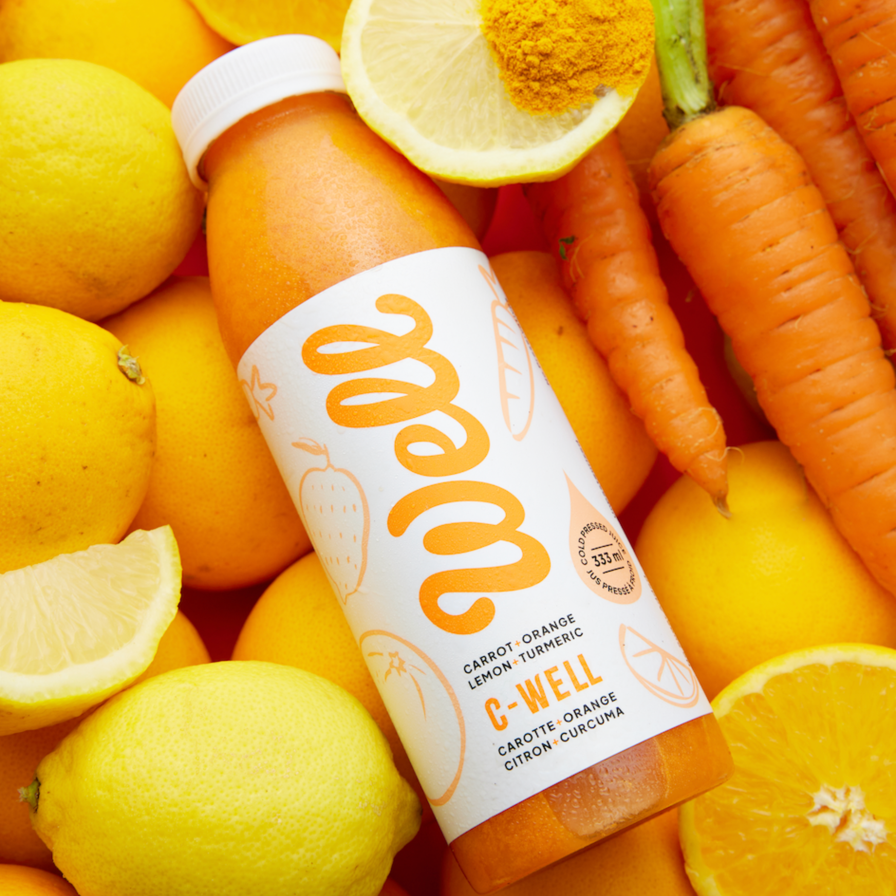 Bottle of C-Well cold pressed juice surrounded by ingredients: carrot, orange, lemon, turmeric