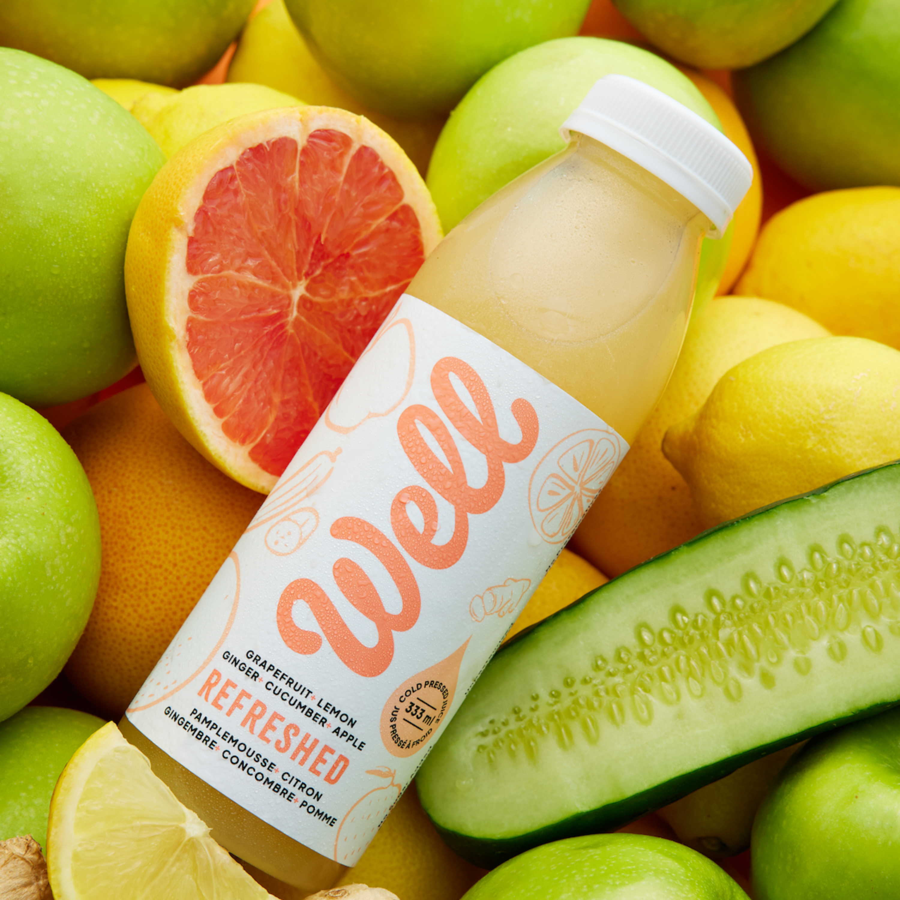 Bottle of 'Well' juice surrounded by fruits and vegetables: grapefruit, lemon, ginger, cucumber, apple